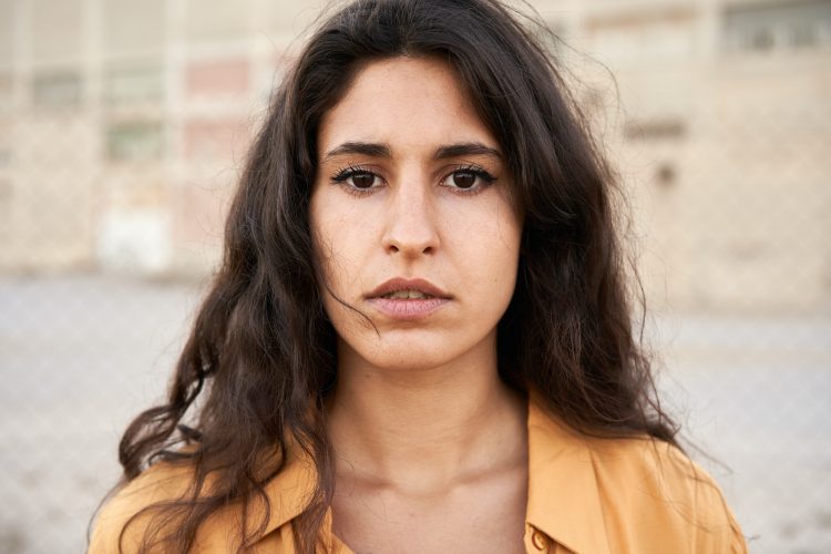 Confident young woman with dark eyes looking at camera with serious expression on her face.