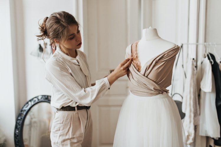 Designer woman creates beige dress. Charming dark-haired lady in white blouse and stylish pants wor