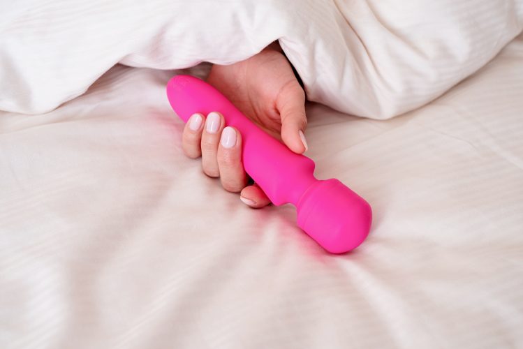 Female hand holding pink vibrator in bed