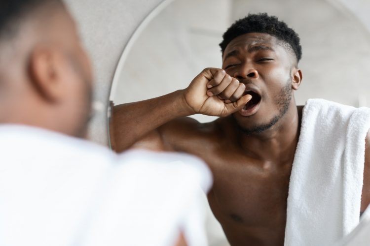 Sleepy African American Man Yawning Standing Near Mirror In Bathroom