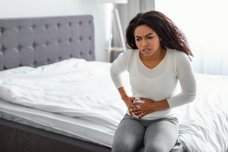 Woman with right side pain sitting on bed at home