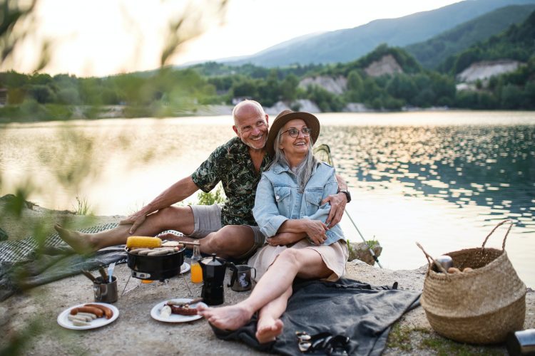 Happy senior couple resting on summer holiday trip, barbecue by lake