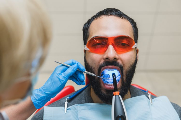 Man`s patient`s tooth teeth while client wearing red protective glasses during operation