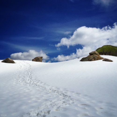 Snowy landscape with footprints forming a path and blue sky