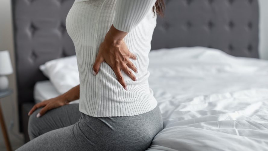 Woman with side back pain sitting on bed at home