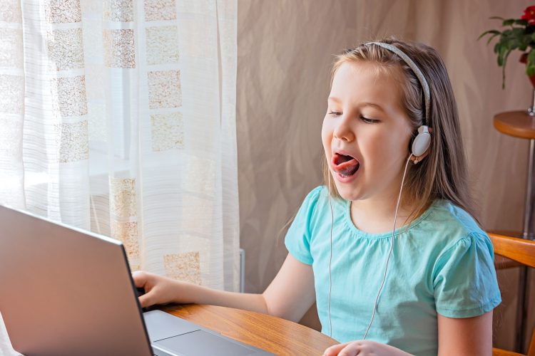 Speech training concept. Little girl uses a laptop to study at home with a teacher, a speech therapi