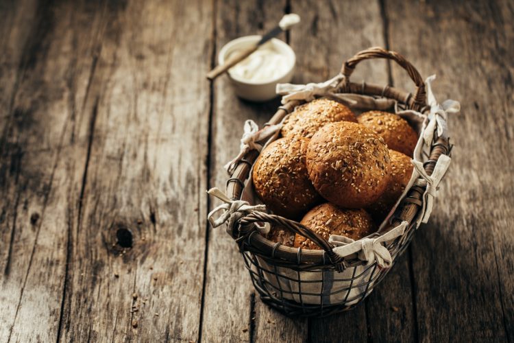 Whole grain bread rolls in a basket on a rustic wooden background.