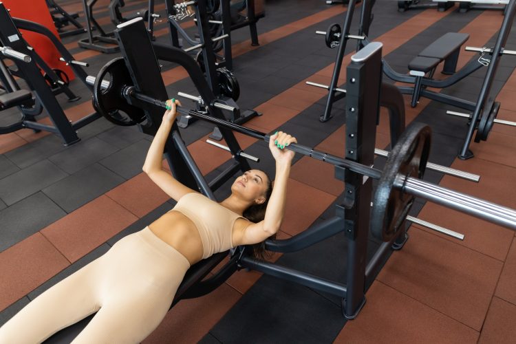 Woman pressing the barbell while lying down during training in the gym