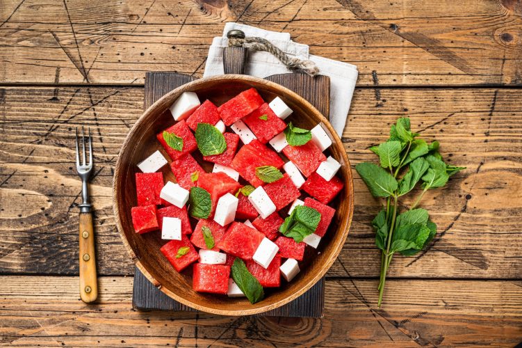 Summer Watermelon Salad with feta cheese and mint in a wooden plate. Wooden background. Top view