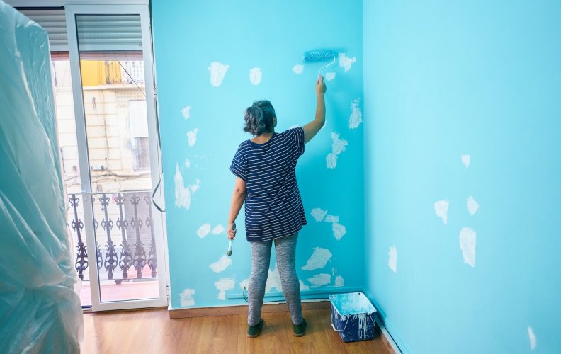 Woman painting a wall cyan color with a roller in a house