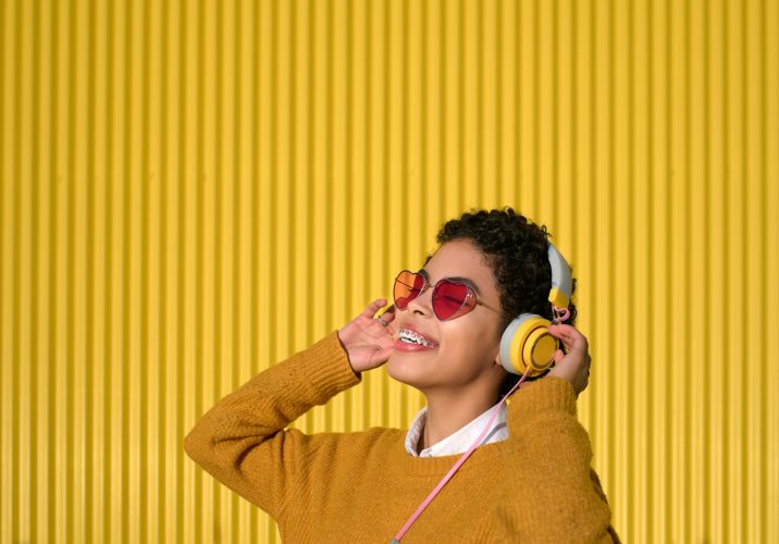 Young Afro-Latina woman listening to music with headphones on yellow background