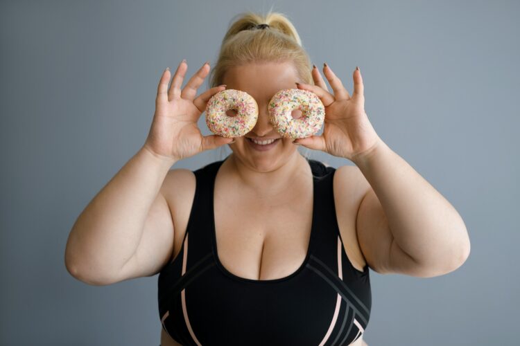 An obese fat woman covers her face with donuts in sweet glaze.