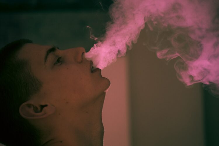 teen boy smokes vape exhales big puffs of smoke