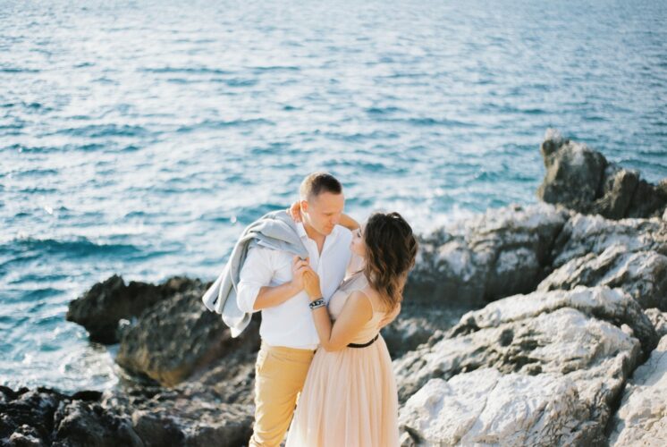 Bride hugs groom by the neck on the rocks by the sea