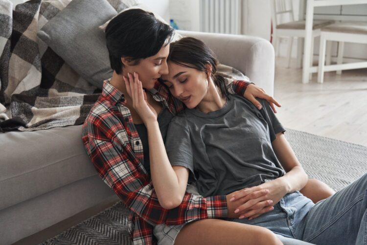 Lesbian couple in love hugging relaxing at home together sitting on floor.