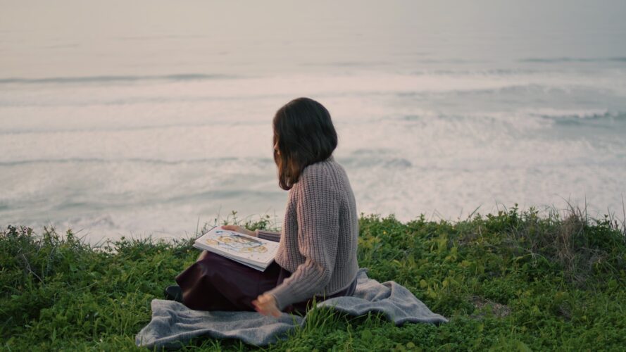 Woman sitting seashore blanket reading book at dramatic sea view. Girl resting.