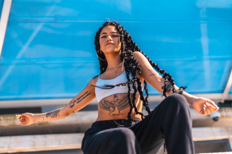 Young Hispanic woman with long braids and tattoos posing under the sunlight
