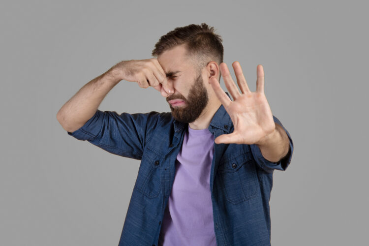 Terrible smell. Millennial hipster guy closing his nose and gesturing STOP, feeling disgusted on