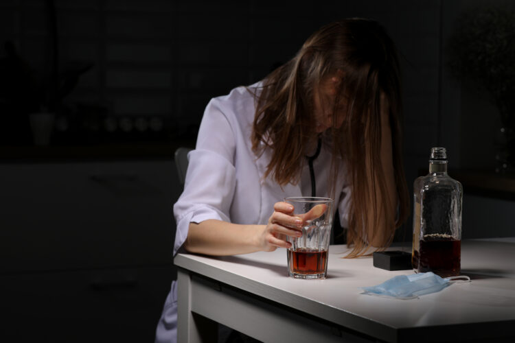 young female doctor drinking alcohol in the kitchen.woman suffering from strong headache or migraine