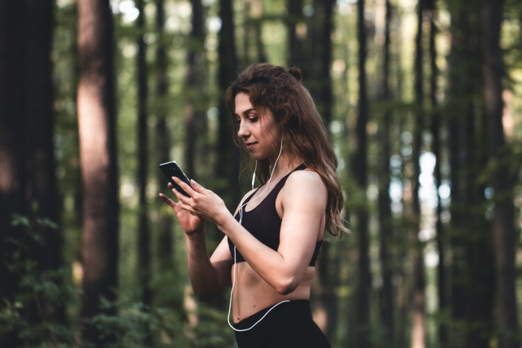 Girl in sports uniform using heahones and looking at phone. Physical activities in nature