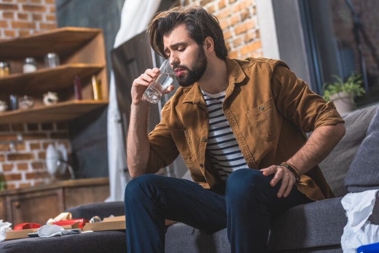 handsome loner drinking water while having hangover in morning at living room